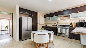 A modern kitchen with a central island, stainless steel appliances, and a dining area with white chairs.