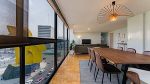 A modern living room with a dining area, large windows, and a view of a cityscape.