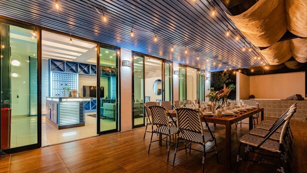 A spacious dining area with a wooden table and striped chairs, a kitchen visible through glass doors, and a ceiling with exposed beams and string lights. - Ideal for Groups, Rooftop, BBQ, Walk to Reforma (Ciudad de México)