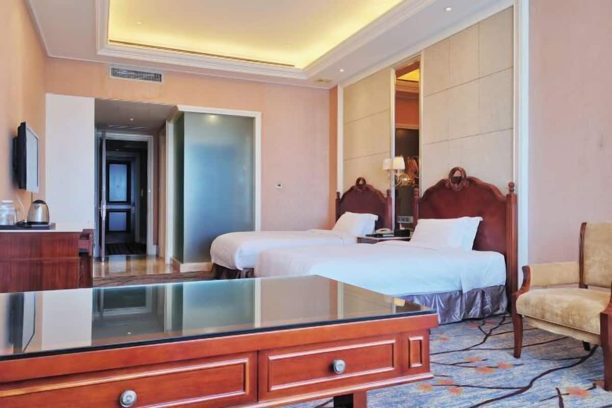 Een hotelkamer met een grote spiegel, twee bedden, een houten dressoir, een stoel en een badkamer die door een open deur zichtbaar is.