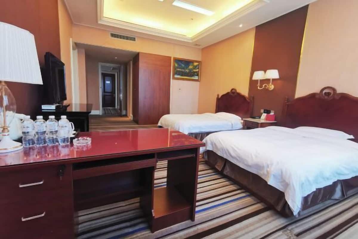 Een hotelkamer met een bureau, twee bedden, een televisie en een schilderij aan de muur.