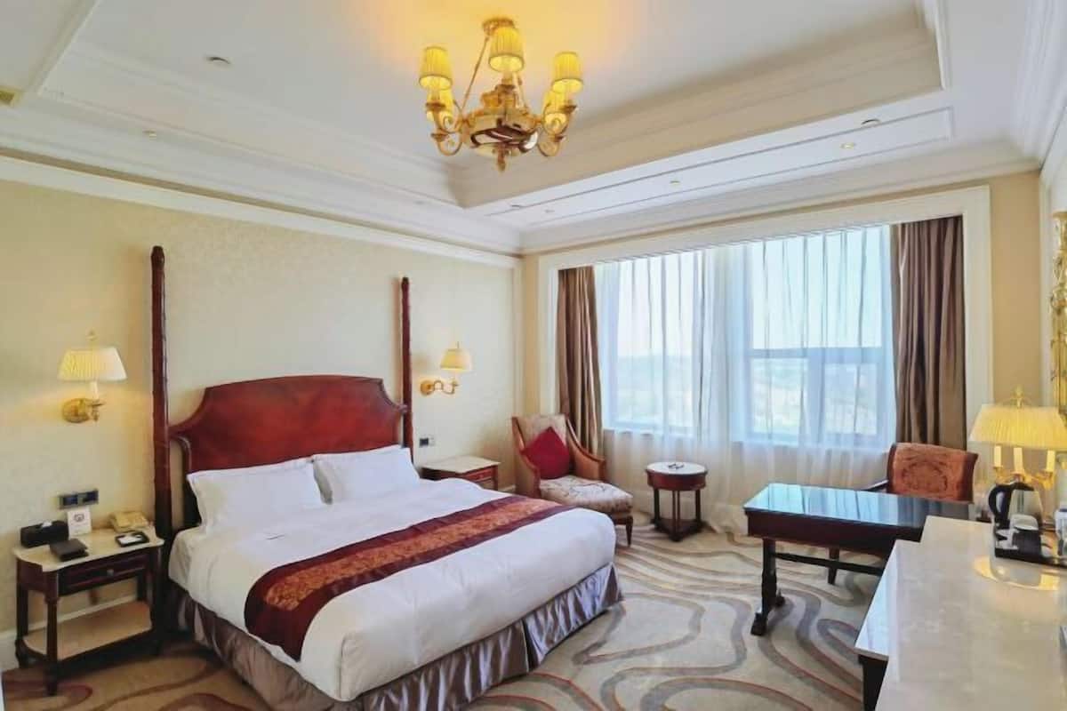 Een hotelkamer met een groot bed, een bureau, een stoel, een klein tafeltje, een lamp, een telefoon en een kroonluchter.
