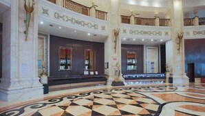 Un'imponente hall con pavimento a scacchi, colonne decorate e soffitto alto.