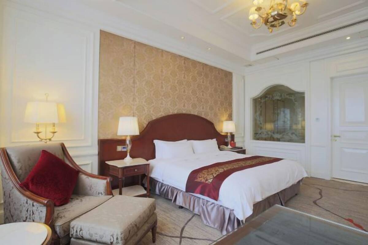Een hotelkamer met een groot bed, twee nachtkastjes met lampen, een rode stoel, een kleine tafel en een kroonluchter.