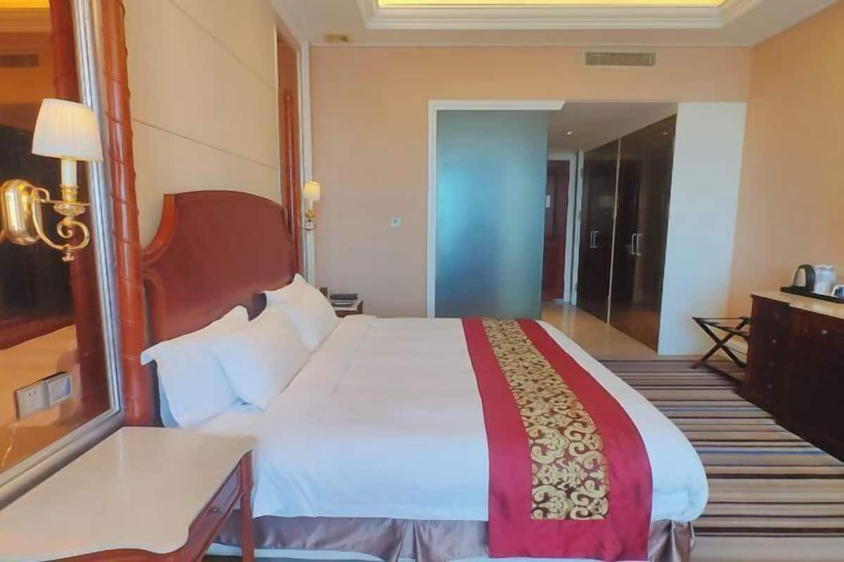 Een hotelkamer met een groot bed, een nachtkastje, een lamp, een kledingkast en een spiegel.