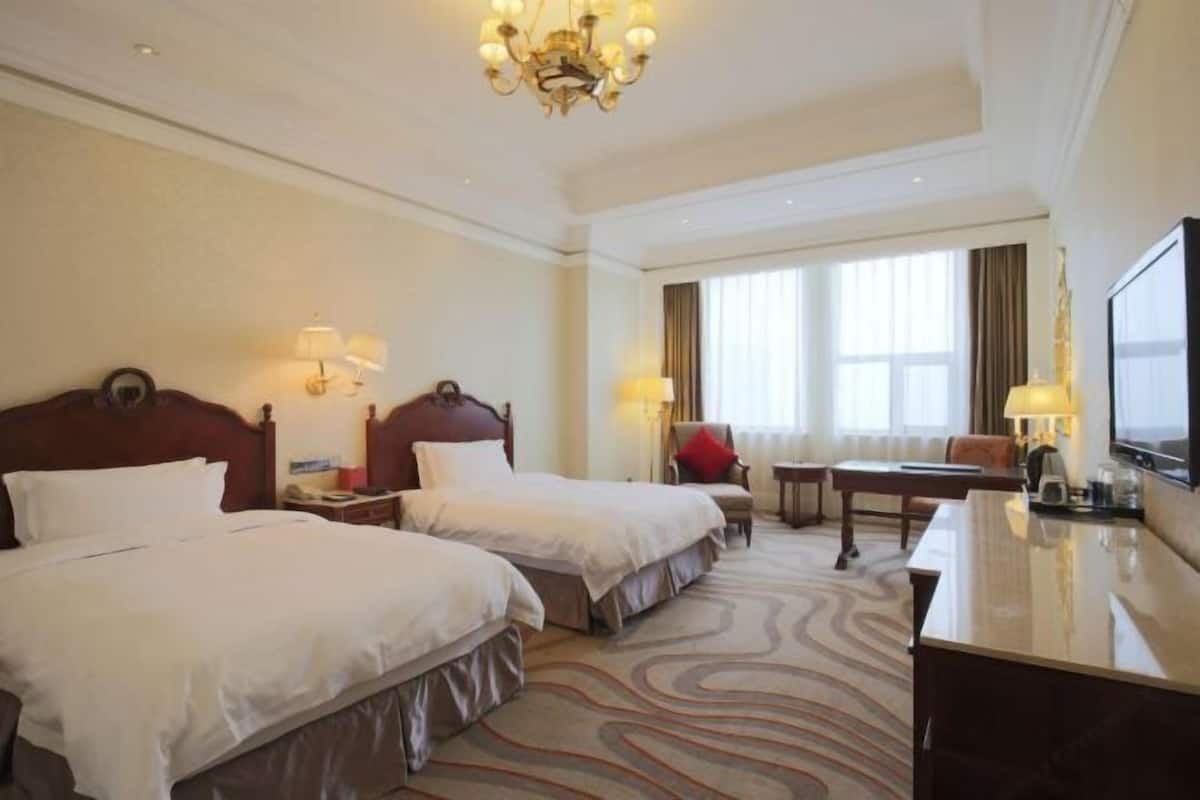 Een hotelkamer met twee bedden, een bureau, een stoel, een televisie en een kroonluchter.