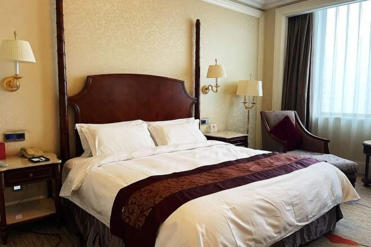 Een hotelkamer met een groot bed, twee nachtkastjes, een stoel en een raam met gordijnen.