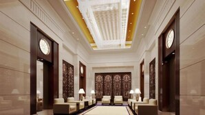 Una hall d'hotel con un'area salotto centrale, lampadari e un soffitto decorato.
