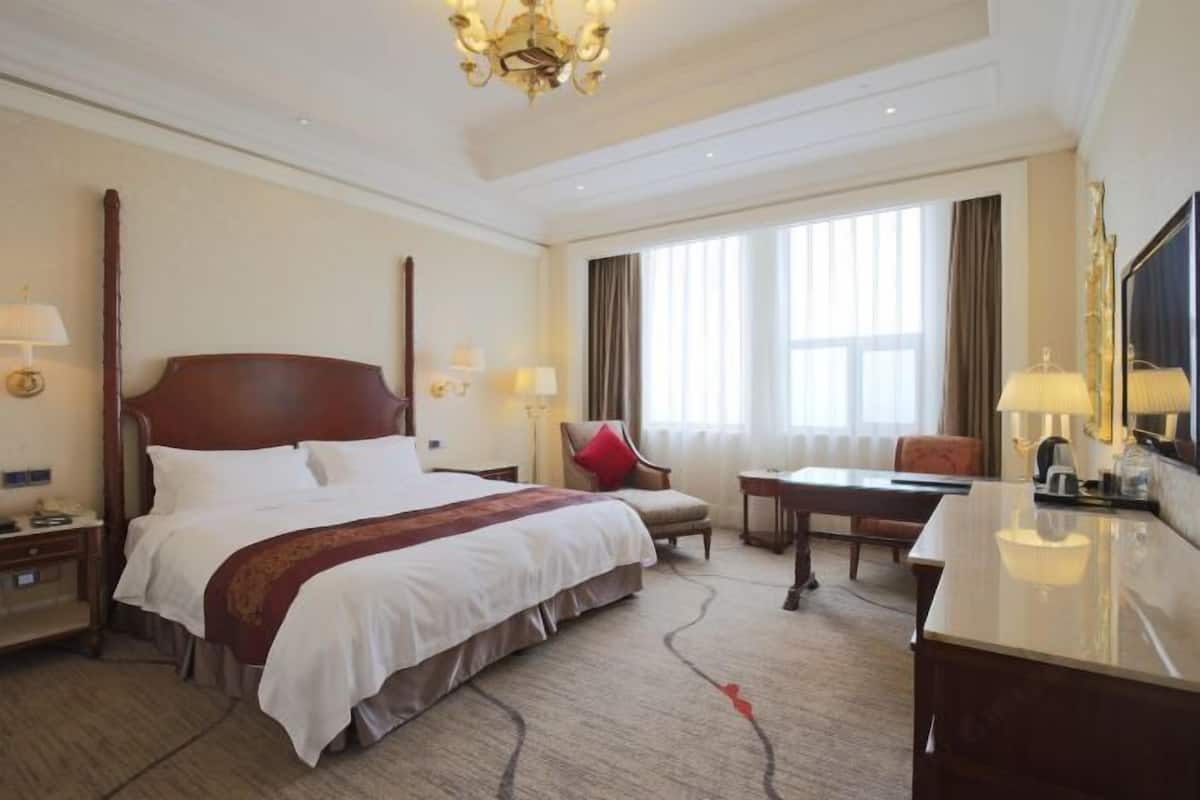 Een hotelkamer met een groot bed, een bureau, een stoel, een televisie en een kroonluchter.