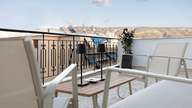 A rooftop terrace with a pool, white lounge chairs, and a table with a lamp.