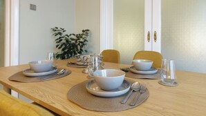 A dining table set with bowls, spoons, and glasses, with a chair and a plant in the background.