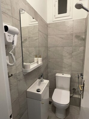 A bathroom with a white toilet, a sink, a mirror, and a hairdryer mounted on the wall. - Athens Koukaki Penthouse, Acropolis view, large veranda (Athens)