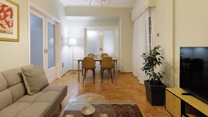 A living room with a sofa, a dining table with chairs, a TV, and a potted plant.