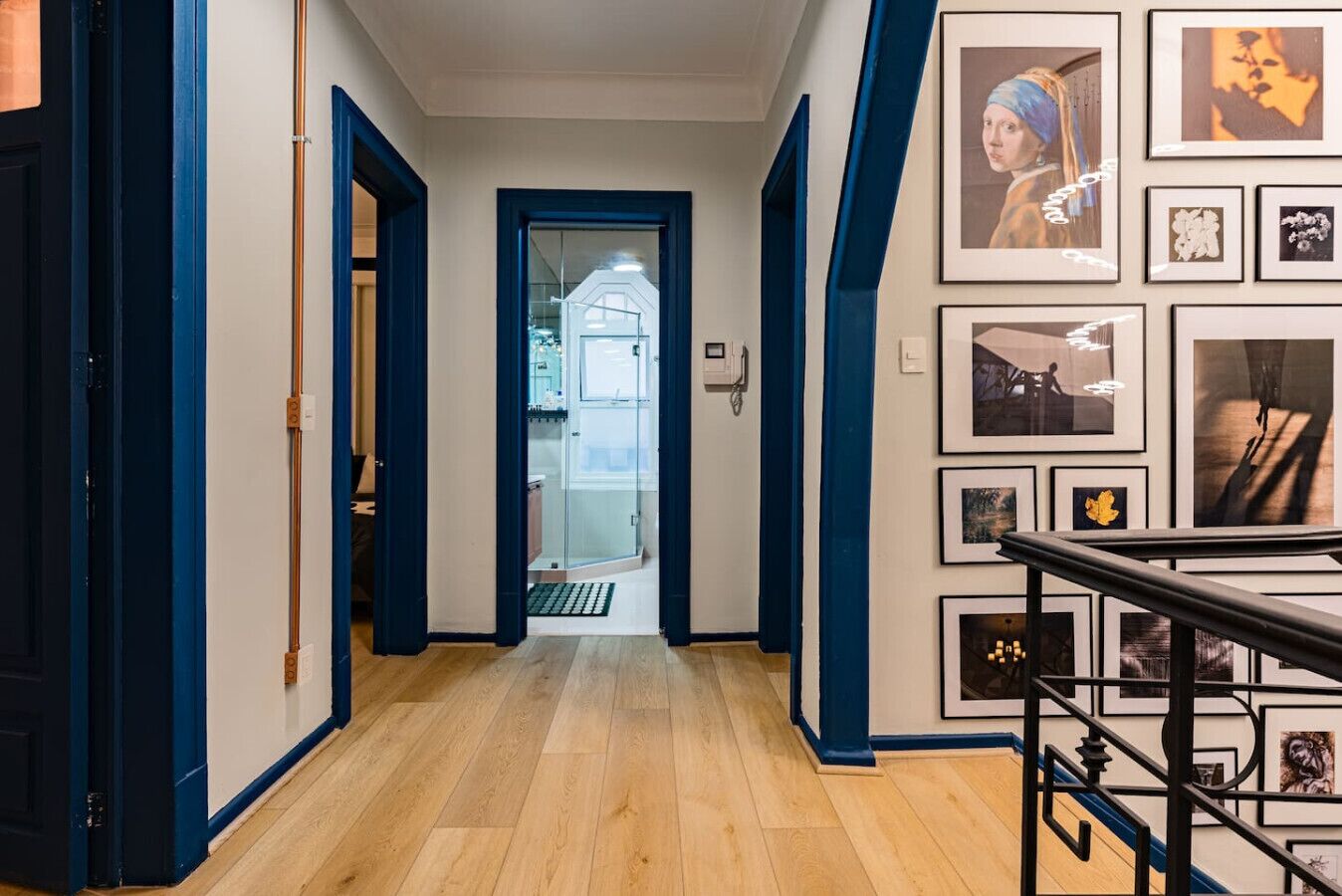 A hallway with wooden flooring, blue walls, and a glass door leading to a kitchen area.