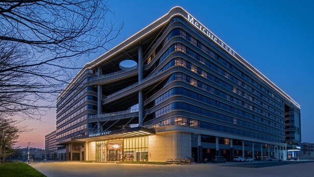 A multi-story hotel with a modern design, featuring a prominent entrance and a covered parking area. - Mercure Guangzhou Baiyun International Airport (Guangzhou)