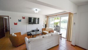 A living room with a white sofa, wicker armchair, and a flat-screen TV mounted on the wall. - Beautiful vacation home in Costa Blanca Golf & Villas by Decameron. (Rio Hato)