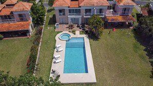 A large rectangular swimming pool with a hot tub, surrounded by a grassy lawn and a wooden deck. - Beautiful vacation home in Costa Blanca Golf & Villas by Decameron. (Rio Hato)