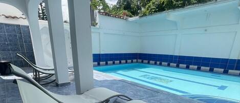 A swimming pool area with lounge chairs and a tiled floor.