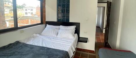 Une chambre à coucher avec un lit, une fenêtre, une table de chevet et une vue sur les bâtiments environnants.