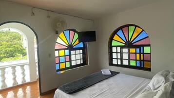 Un dormitorio con cama, ventana con vidrio de colores, ventilador de techo y balcón.
