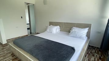 A bedroom with a large bed, wooden floor, and a wooden ceiling beam.