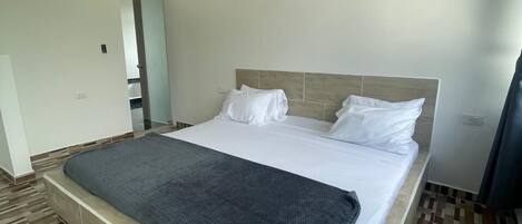 A bedroom with a large bed, wooden floor, and a wooden ceiling beam.