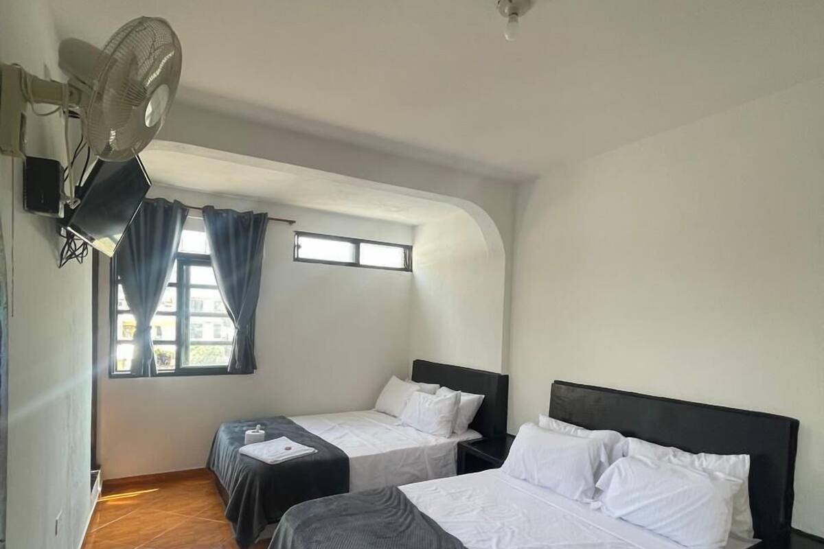 Une chambre d’hôtel avec deux lits, un ventilateur de plafond, une fenêtre avec des rideaux et un sol carrelé.