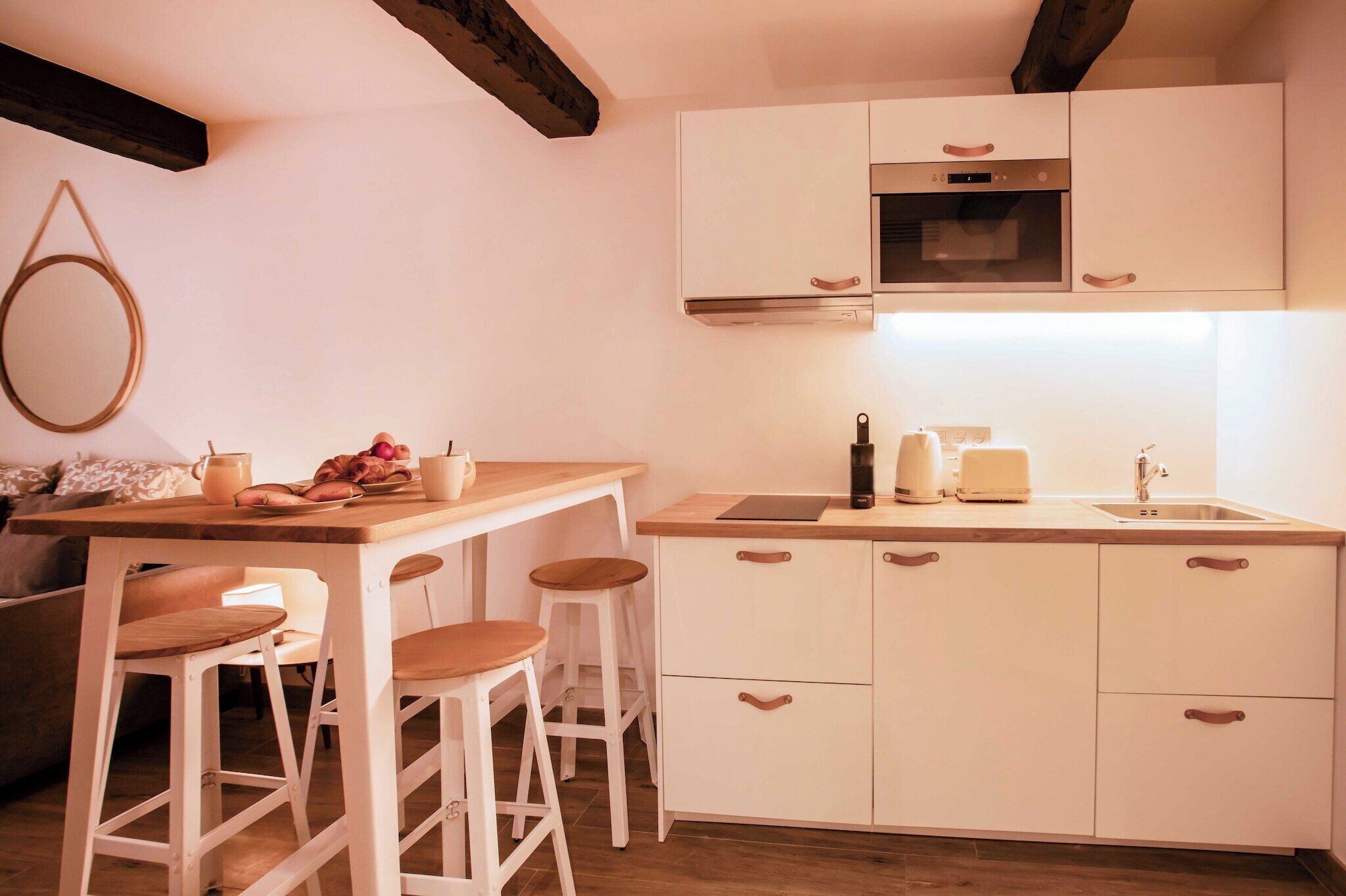 Une cuisine avec des meubles blancs, un plan de travail en bois, un évier et deux tabourets.