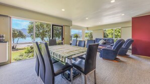 A dining area with a table and chairs, large windows with a view of the sea, and a red accent wall.