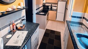 Una cucina compatta con un piano di lavoro nero, un frigorifero bianco e mobili in legno.