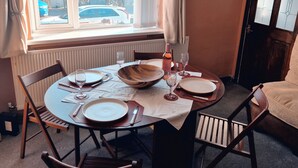 Zona pranzo con tavolo imbandito per quattro persone, una finestra con tende e vista all'esterno.