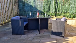 Un'area patio con un tavolo e quattro sedie, un bicchiere di vino e una bottiglia sul tavolo.