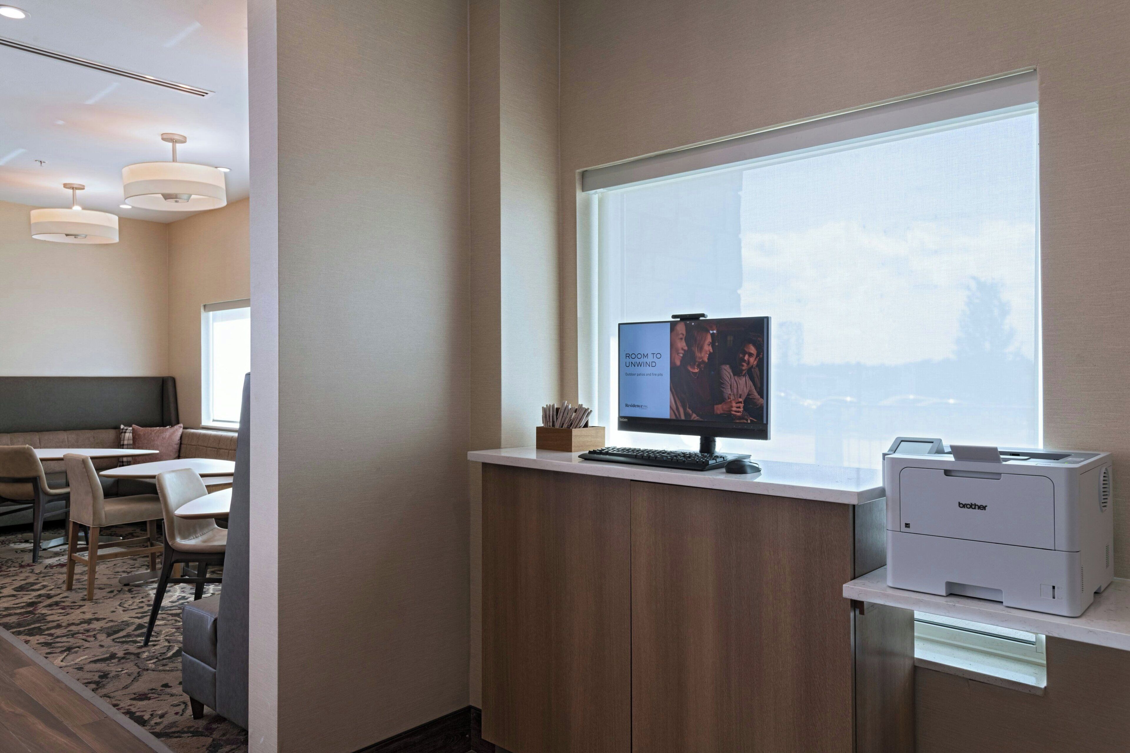 A modern office space with a desk, computer, printer, and a window with a view.