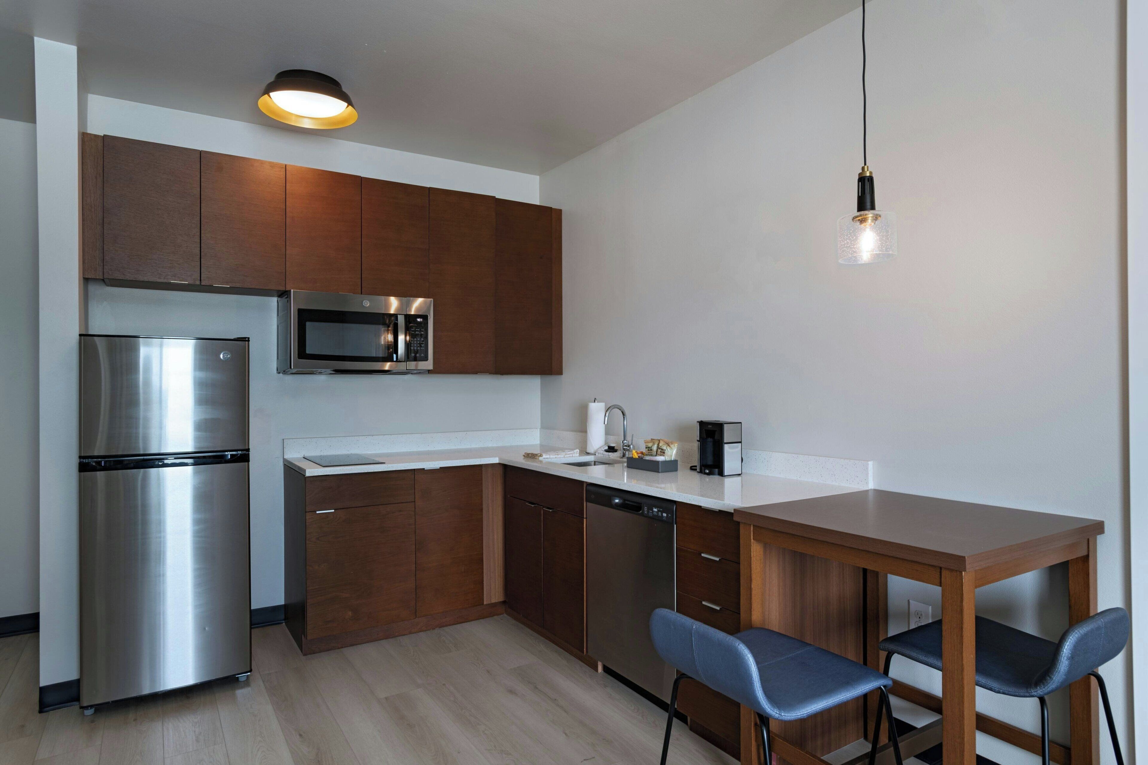Une cuisine moderne dotée d’appareils électroménagers en acier inoxydable, de meubles de rangement en bois et d’une table à manger en bois accompagnée de deux chaises.
