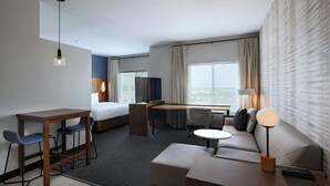 Una habitación de hotel moderna con cama, escritorio, zona de estar y ventanas amplias.