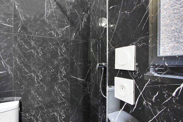 A bathroom with black marble walls, a shower area, and a toilet. - Cozy Studio - 4P - Place de la Bastille (Paris)