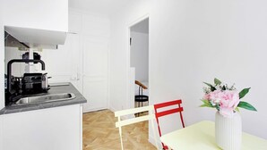 Cocina compacta con un lavamanos, una cafetera y una silla cerca de una mesa de comedor con un florero.