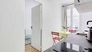 Una cocina compacta con ventana, un pequeño comedor con mesa y sillas, y una puerta que da a otra habitación.