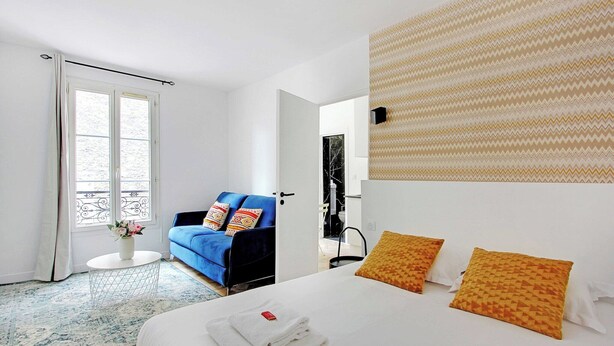 Habitación de hotel con cama, sofá azul, una mesita con un florero y pared con diseño.