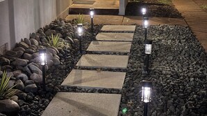 A pathway with stone slabs and gravel, leading to a building entrance with a bench and a tree. - Old-World Charm in Abilene! Spanish Revival Home, Sleeps 8! (Abilene)