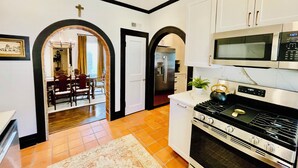 A kitchen with white cabinets, a stove, and a microwave. There is a dining area visible through an archway. - Old-World Charm in Abilene! Spanish Revival Home, Sleeps 8! (Abilene)