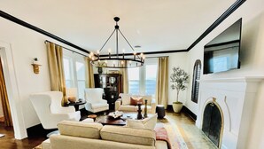 A spacious living room with a chandelier, a fireplace, and a television mounted on the wall. - Old-World Charm in Abilene! Spanish Revival Home, Sleeps 8! (Abilene)
