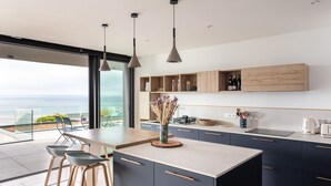 A modern kitchen with a large island, bar stools, and a view of the ocean. - La Briouette - avec vue panoramique d’exception (Pléneuf-Val-André)