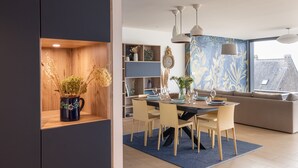 A modern dining area with a wooden shelf, a dining table set with plates, glasses, and a vase of flowers. - La Briouette - avec vue panoramique d’exception (Pléneuf-Val-André)