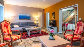A living room with a sofa, chairs, a coffee table, and a TV. There is a staircase leading to another room. - Hon Ty Glas - Maison proche de plage avec jardin (Moëlan-sur-Mer)