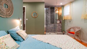 A bedroom with a bed, a wicker chair, a shower area, and a mirror. - Hon Ty Glas - Maison proche de plage avec jardin (Moëlan-sur-Mer)