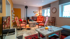 A cozy living room with a fireplace, comfortable seating, and a large window providing natural light. - Hon Ty Glas - Maison proche de plage avec jardin (Moëlan-sur-Mer)