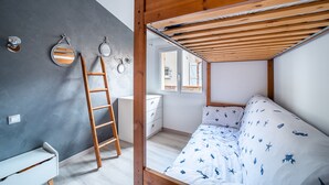 A bedroom with a bunk bed, a ladder, a desk, and a window with a view.