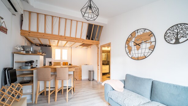 A compact living space with a kitchenette, a dining area, a sofa, and a loft bedroom.
