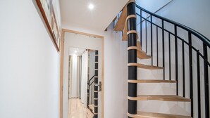 A modern staircase with a wooden handrail and black metal balusters, leading to an upper floor.